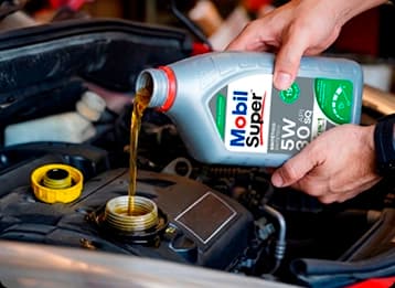 Mãos despejando óleo Mobil Super 5W-30 no motor de um carro durante manutenção automotiva.