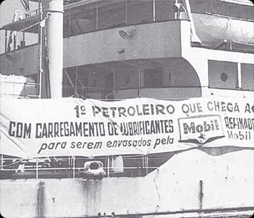 Imagem histórica em preto e branco de navio com faixa sobre carregamento de lubrificantes Mobil.