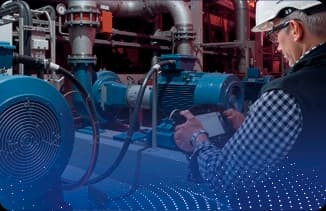 Profissional usando capacete e tablet para monitorar motores e tubulações em ambiente industrial.