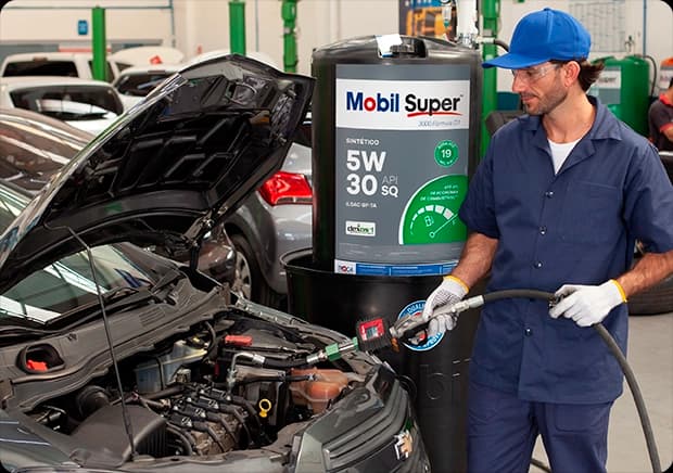 Mecânico abastecendo motor de carro com óleo Mobil Super 5W-30 em oficina automotiva.