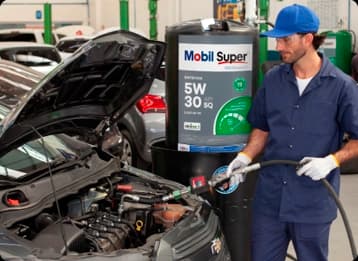 Mecânico abastecendo motor de carro com óleo Mobil Super 5W-30 em oficina automotiva.