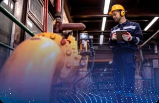 Operador usando capacete e protetor auricular inspecionando tubulações industriais com tablet.