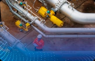 Profissional usando EPI em área industrial com tubulações e equipamentos vistos de cima.