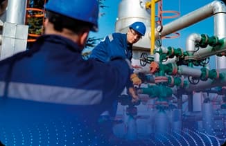 Técnicos usando capacete e uniforme azul realizando manutenção em tubulações industriais.