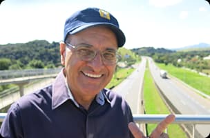 Pedro Trucão, apresentador do Pé na Estrada, usando boné azul e camisa cinza com logo Mobil em fundo escuro.