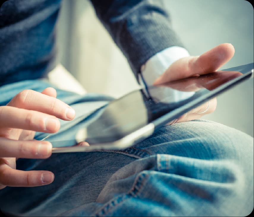 Homem usando tablet apoiado nas pernas com foco nas mãos tocando a tela do dispositivo.