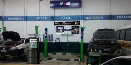 Oficina automotiva com carros em manutenção, elevadores e galão Mobil Super da Troca Inteligente.